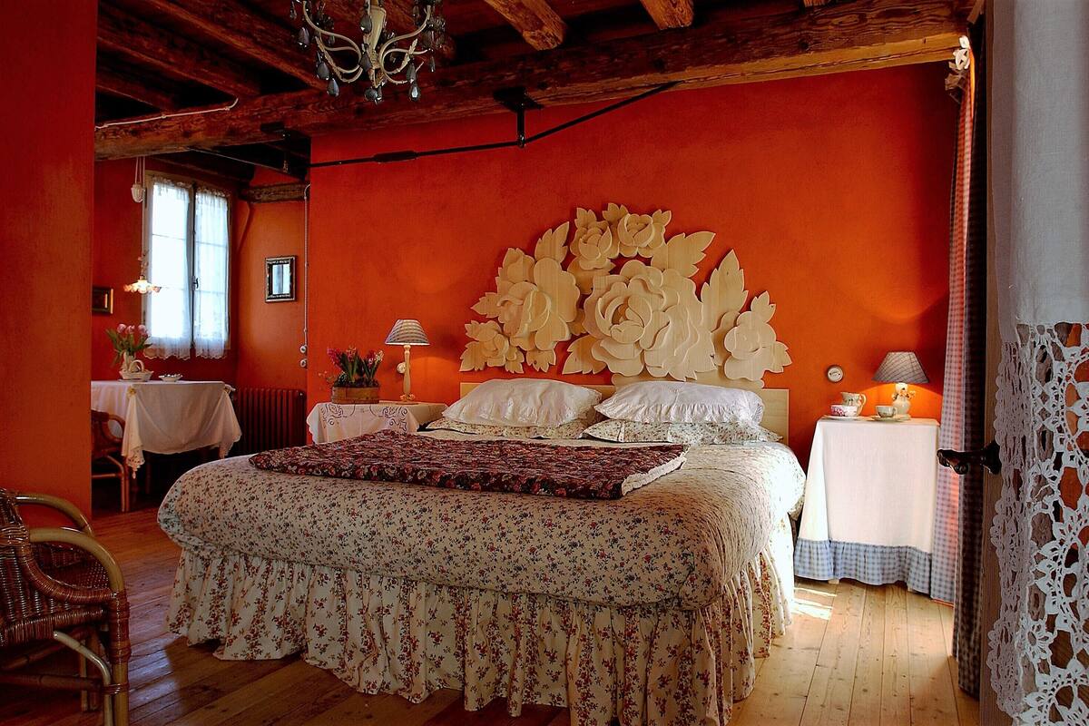 Un dormitorio con una cama grande, ropa de cama floral, techo de madera y una mesa con una lámpara.