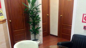 Una habitación con dos sillones blancos, una mesa de centro de vidrio y un sofá negro. Hay una planta en maceta y una puerta de madera con un letrero que dice 'Private'.