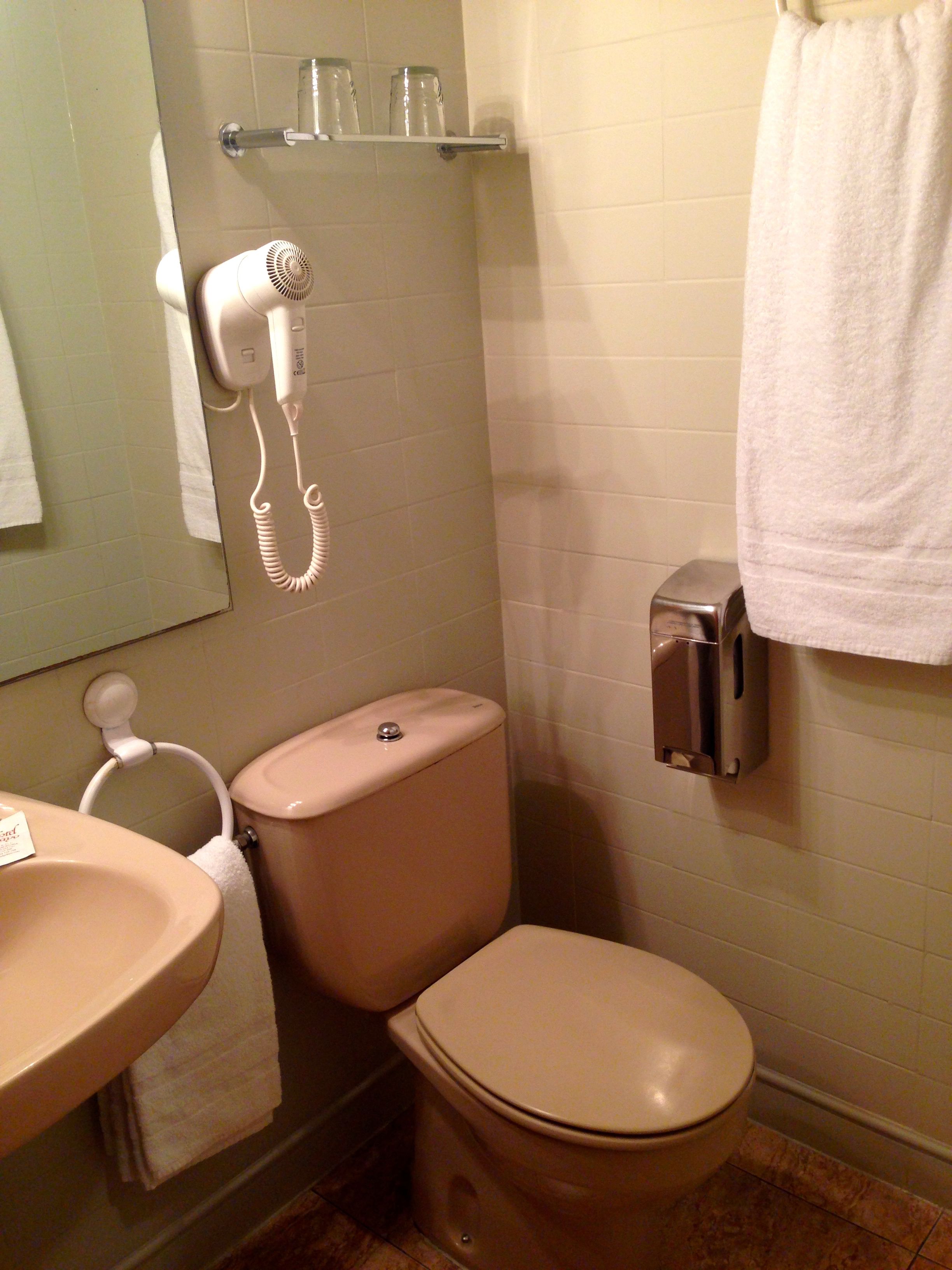 A bathroom with a toilet, sink, and a hairdryer mounted on the wall.