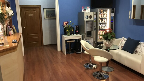 Una habitación con piso de madera, un sofá blanco, una pequeña mesa redonda, una silla blanca, una máquina expendedora y un televisor en la pared.