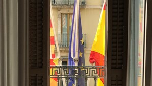 Un balcón con vistas a un edificio, con barandilla y una ventana con contraventanas.