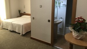 Una habitación de hotel con una cama, un baño con lavamanos y espejo, y una pequeña mesa con una planta.