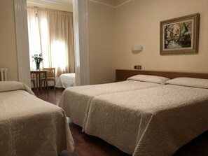 A hotel room with two beds, a desk with a chair, a painting on the wall, and a window with curtains. - Hotel Pelayo (Barcelona)