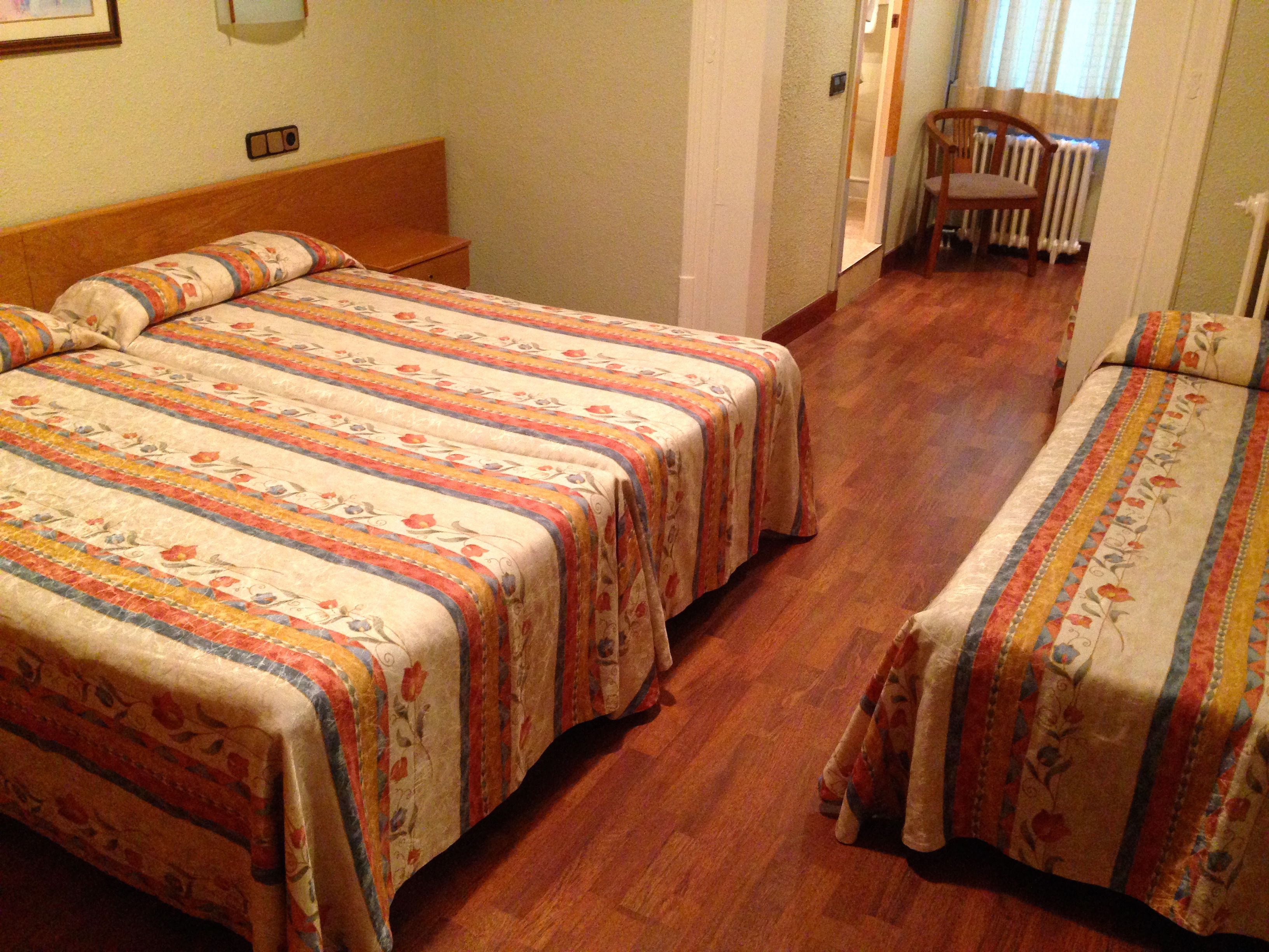 Hotellihuone, jossa on kaksi sänkyä, puulattia, tuoli ja patteri.