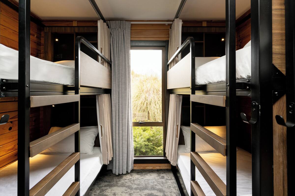 A room with bunk beds, wooden walls, and a window with curtains.
