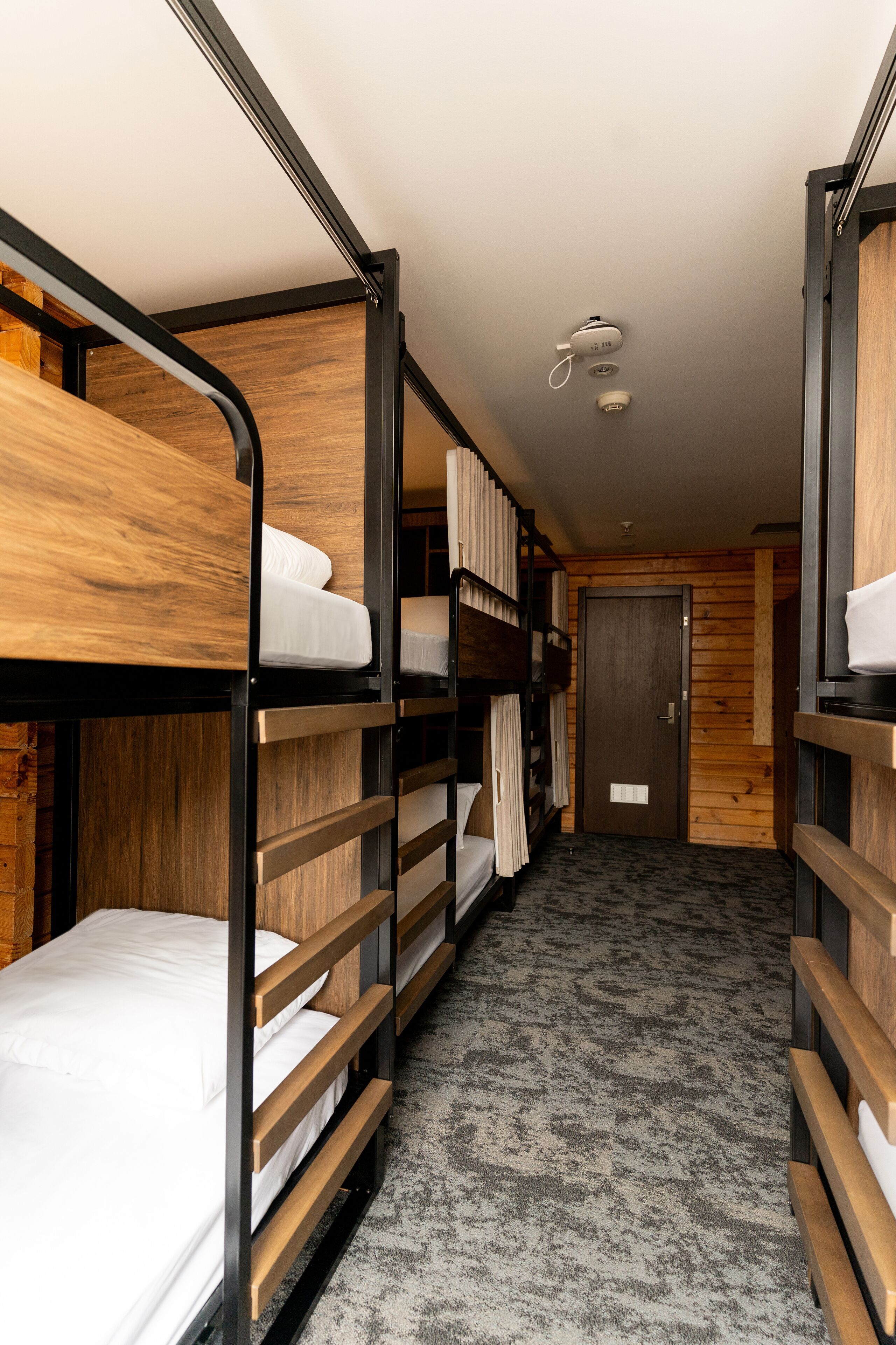 A narrow hallway with bunk beds on either side, a wooden door at the end, and a ceiling light fixture.