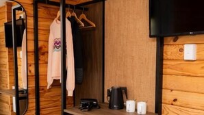 A compact room with a wooden wall, a small desk with a chair, a hanging coat rack, and a television mounted on the wall. - Haka House Hostel – Aoraki Mt Cook (Mount Cook)