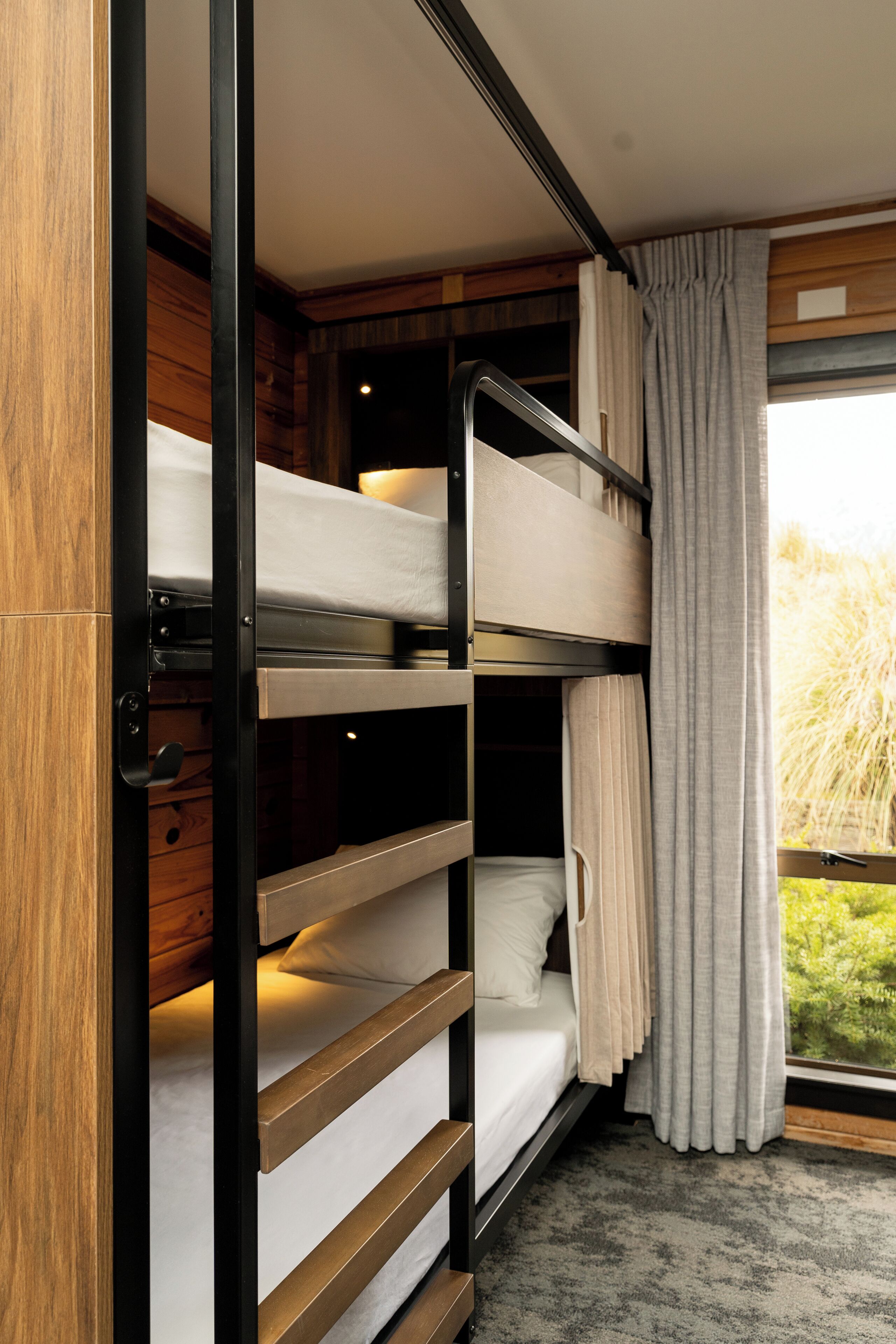 Een slaapkamer met stapelbedden, houten wanden en een raam met gordijnen.