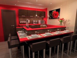 A modern kitchen with red countertops, a dining area with bar stools, and a large painting of a rose. - Les Baladines Residence Tourisme (Thonon-les-Bains)