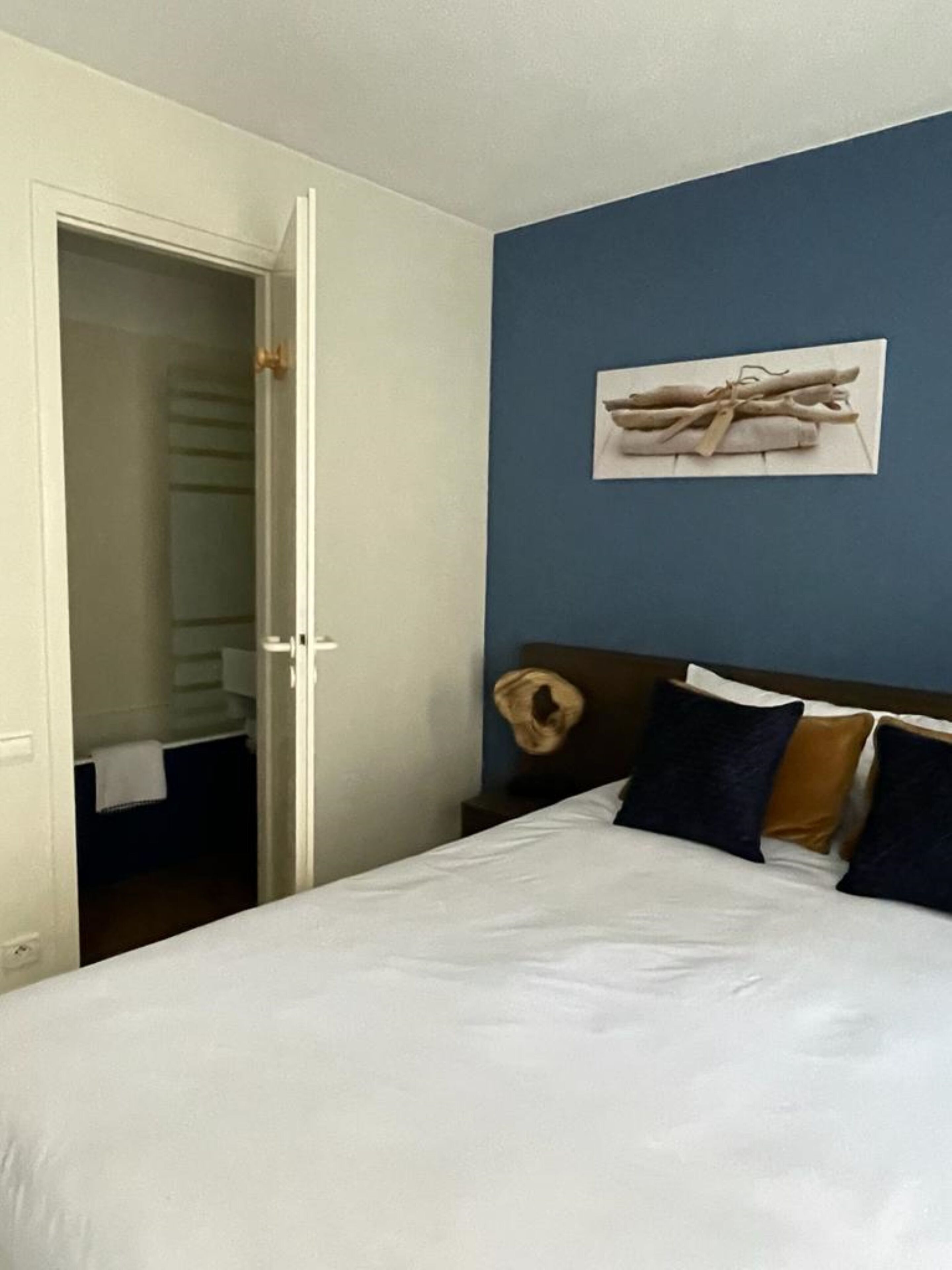 Een hotelkamer met een bed, hoofdeinde, een kunstwerk aan de muur en een kast met een handdoek.