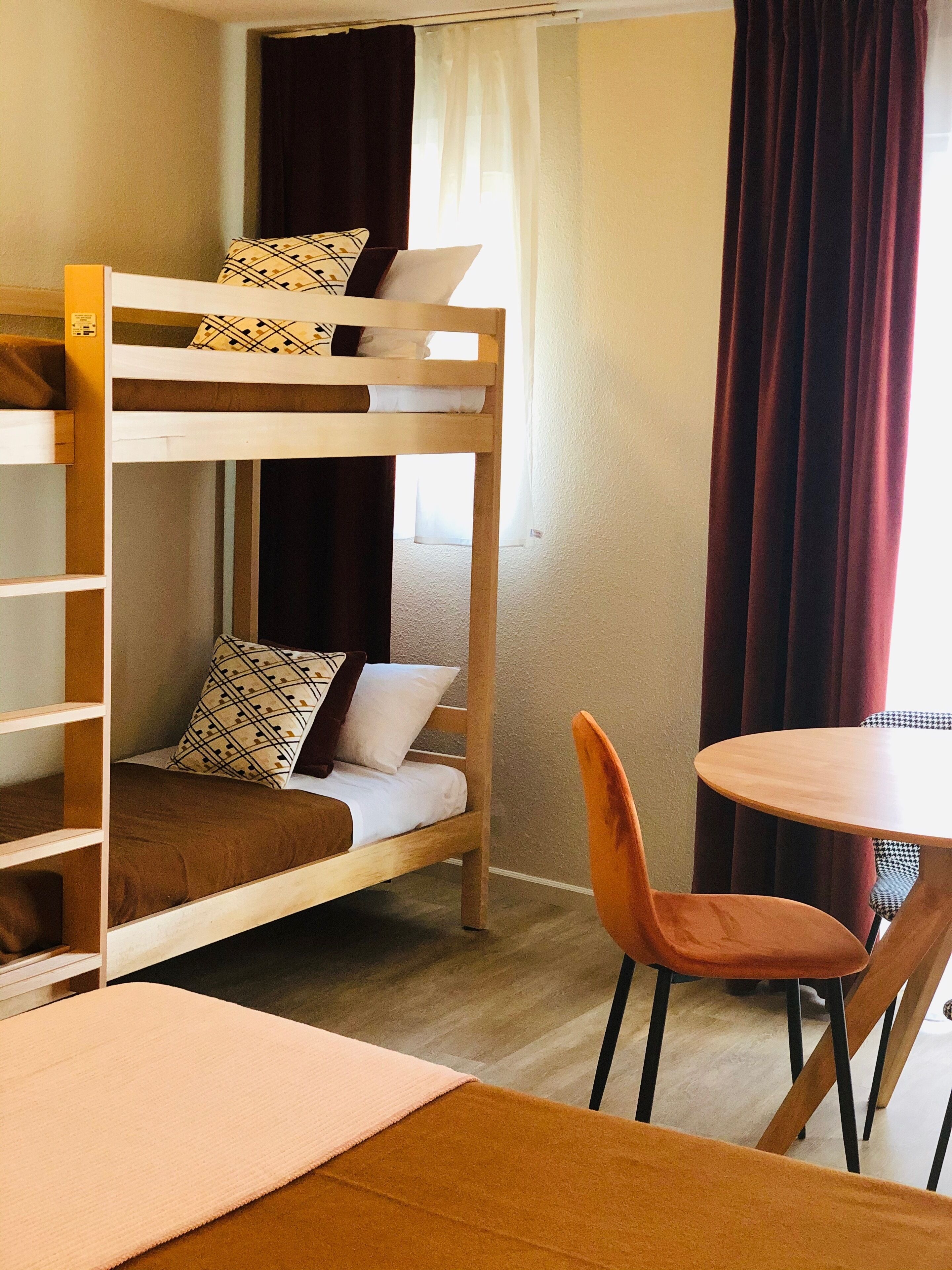 A bunk bed with a table and chairs in a room with a window and curtains.