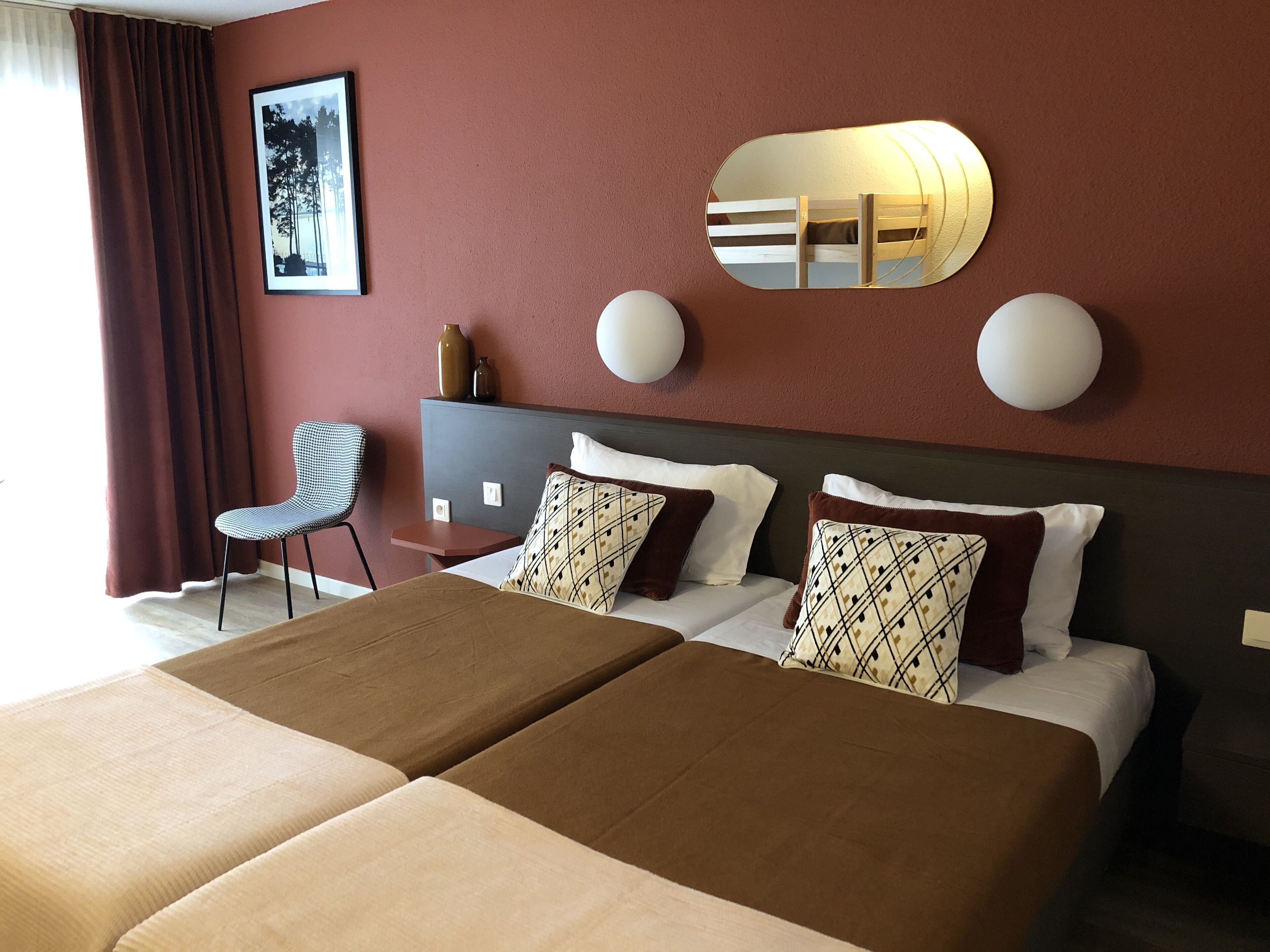 Habitación de hotel con dos camas, un escritorio, una silla y un espejo grande.