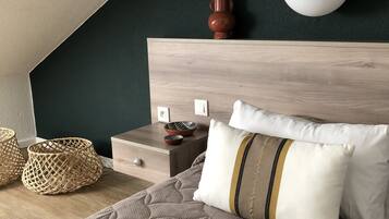 A bedroom with a sloped ceiling, a wooden headboard, a bed with a quilted cover, two woven baskets, a nightstand, a white vase, and a round wall light.