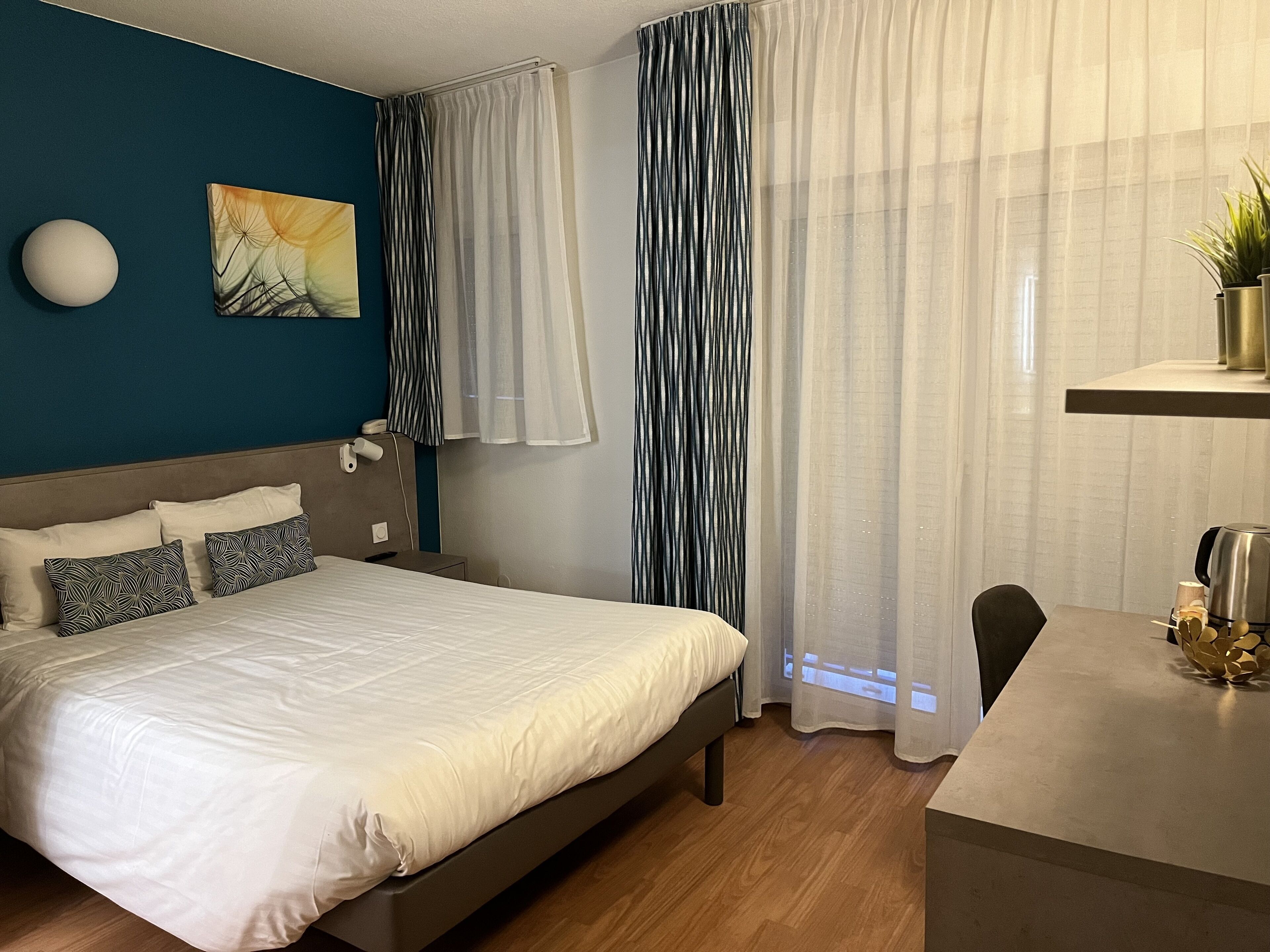Ein modernes Hotelzimmer mit einem Bett, Nachttisch und einem Schreibtisch mit Kaffeemaschine.