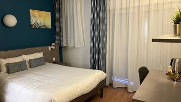 Ein modernes Hotelzimmer mit einem Bett, Nachttisch und einem Schreibtisch mit Kaffeemaschine.