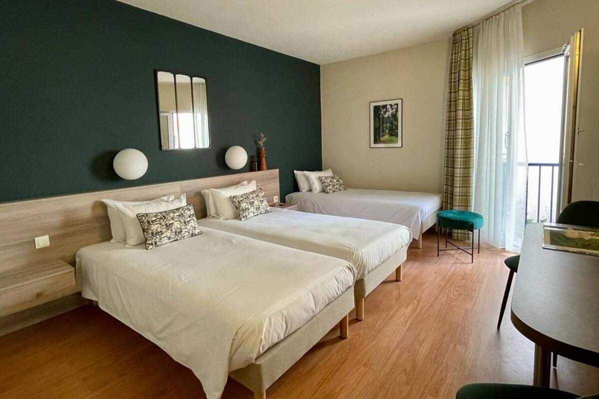 A hotel room with two beds, a dining table, and a view of the outdoors.