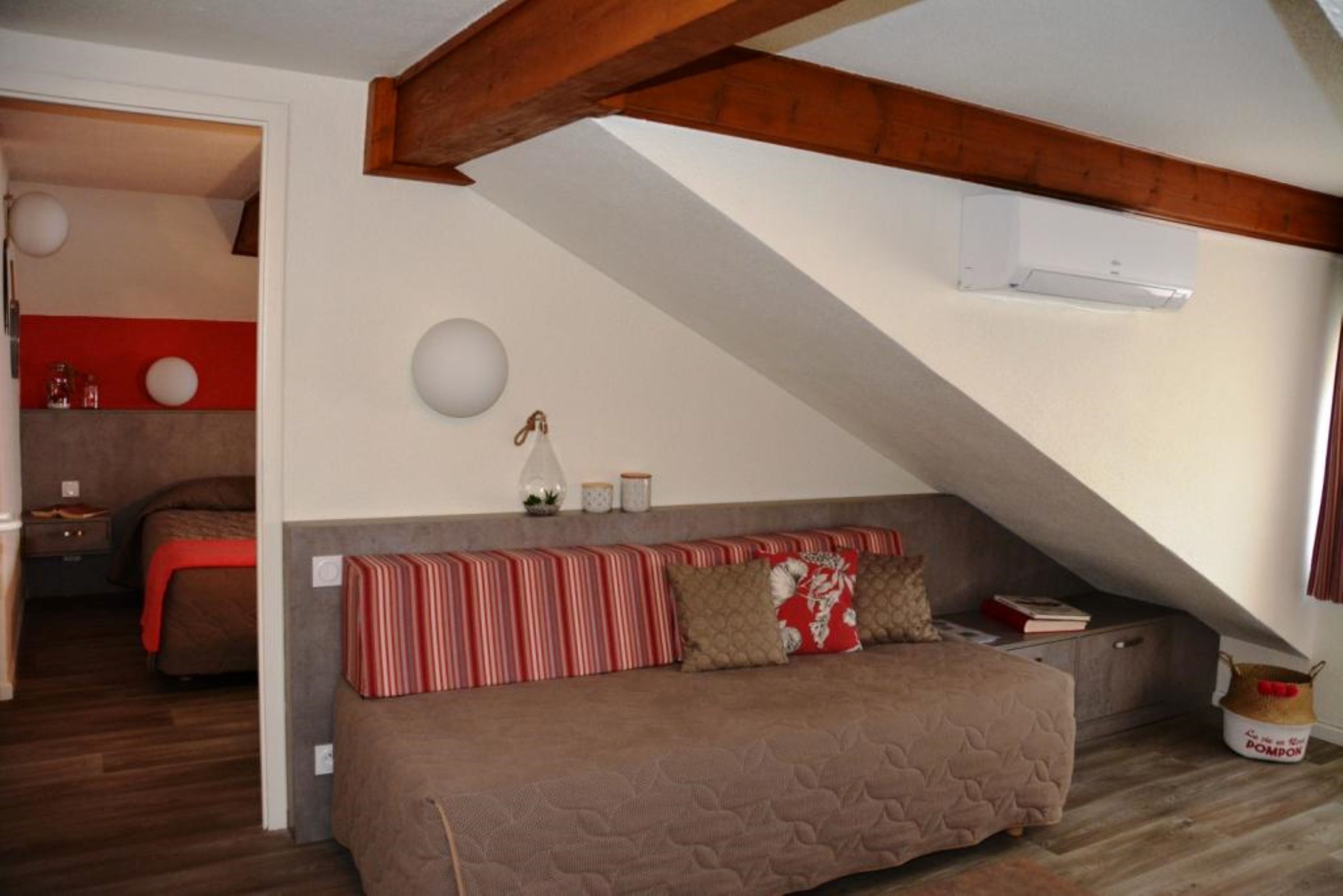 A cozy room with a sloped ceiling, a sofa with striped cushions, a small table with decorative items, and a red accent wall.