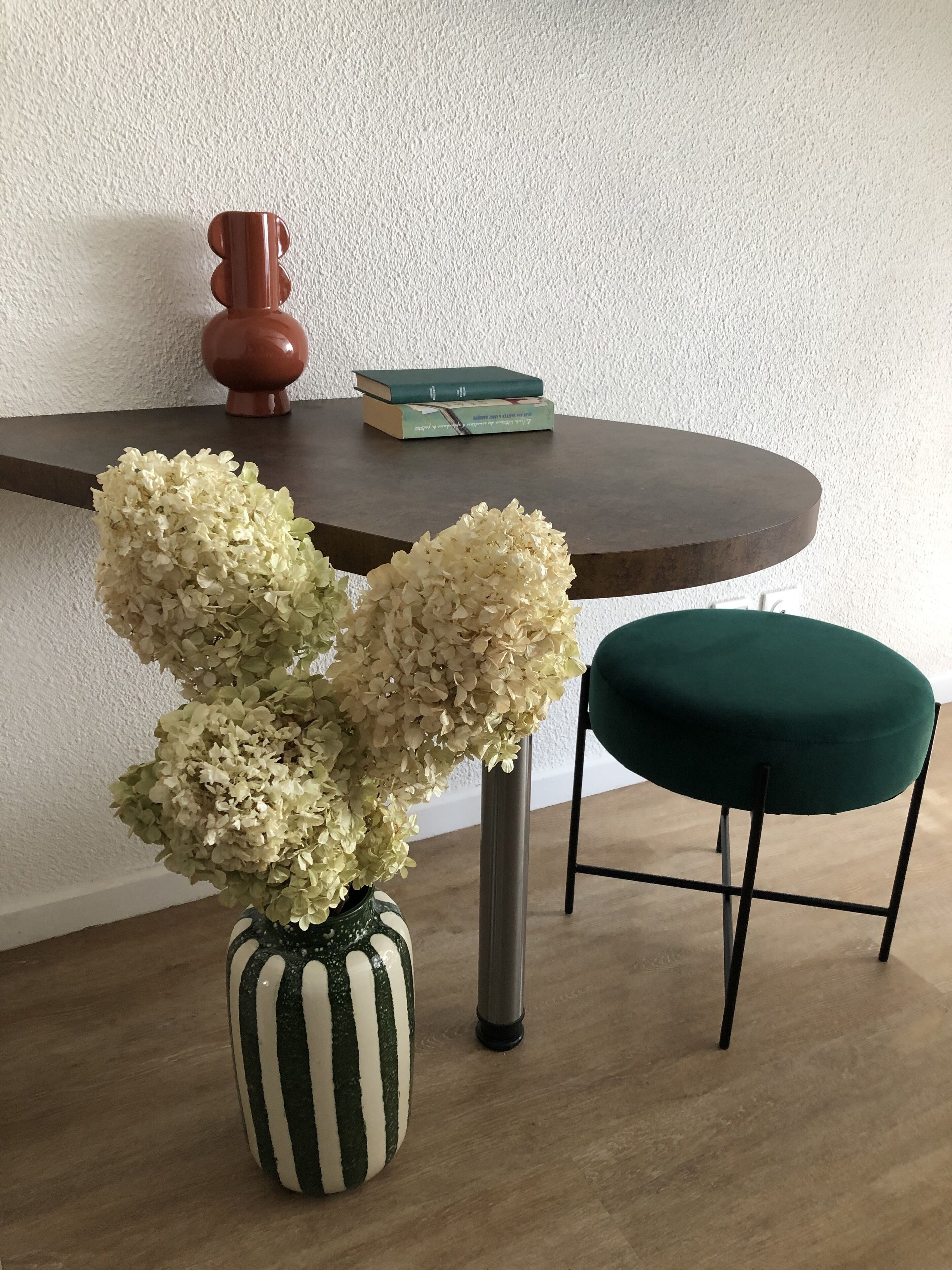 A small table with a vase of white flowers, a book, and a decorative item on a white textured wall.