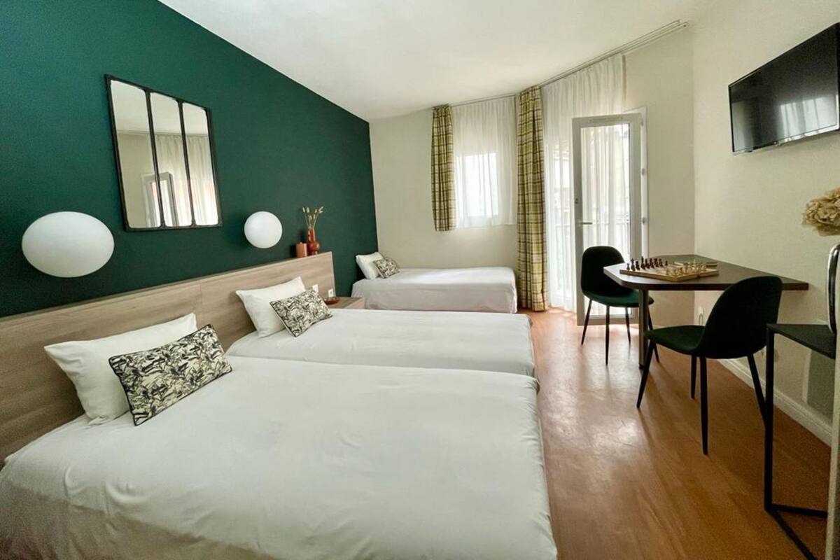 A hotel room with two beds, a desk, a chair, a TV, and a window with curtains.