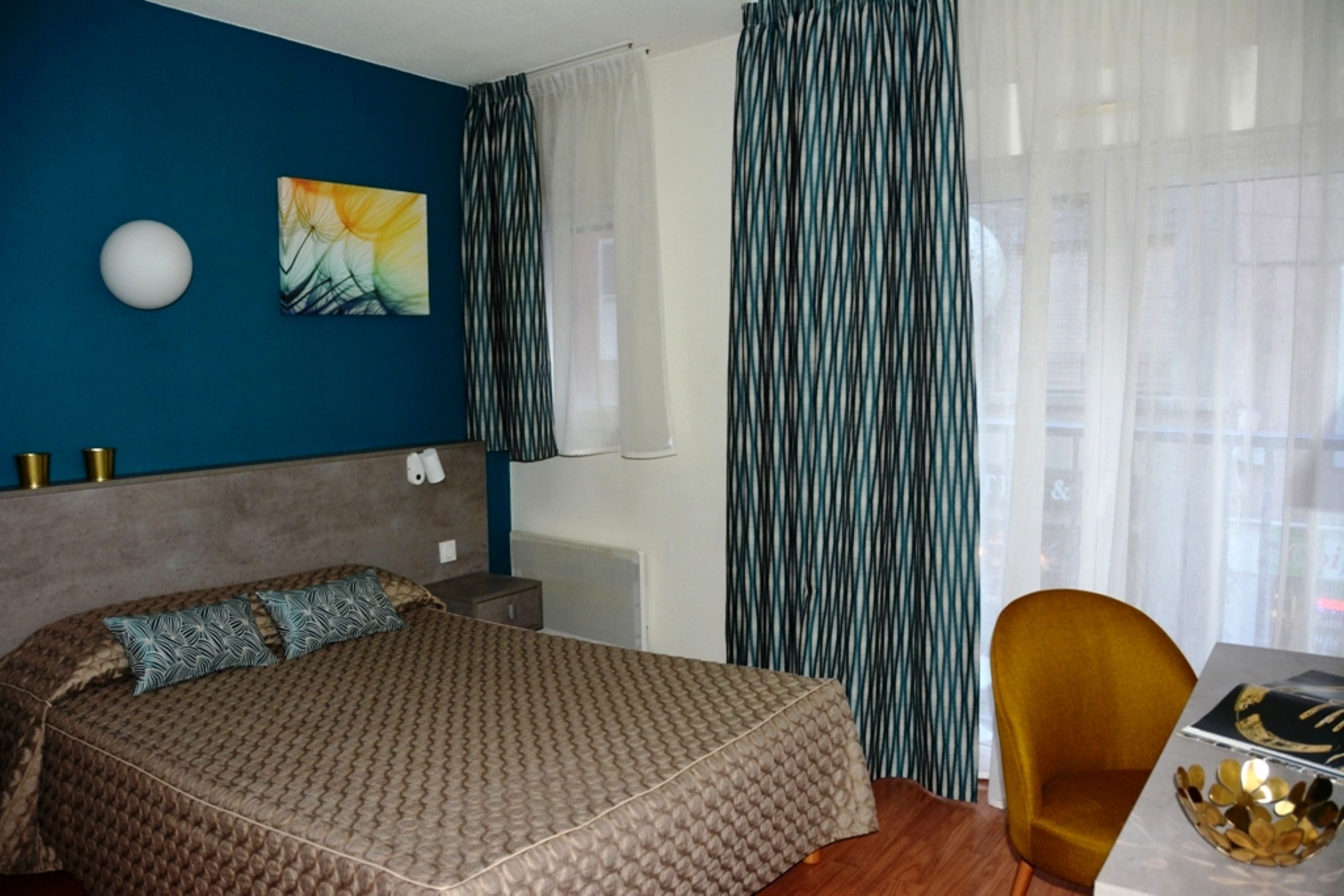 Un dormitorio con cama, una silla, una mesa, un cuadro y cortinas.