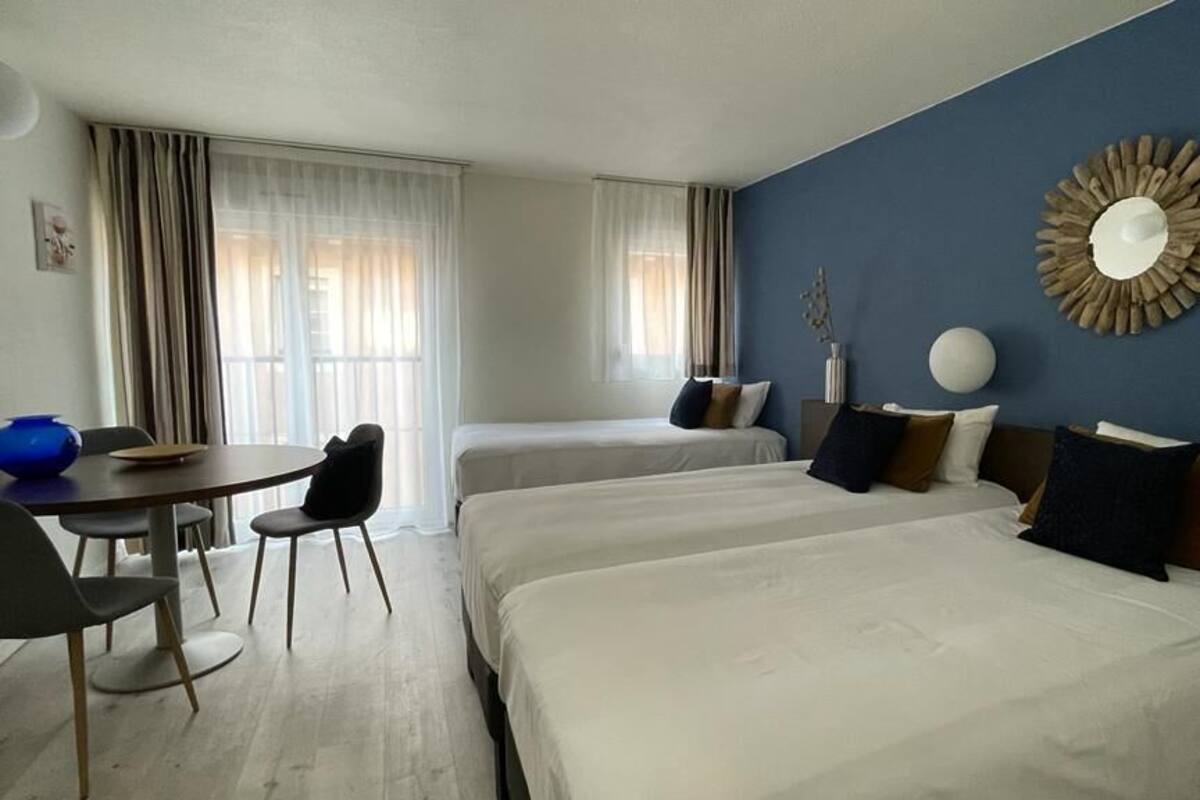 A hotel room with two beds, a dining table with chairs, and a large mirror on the wall.