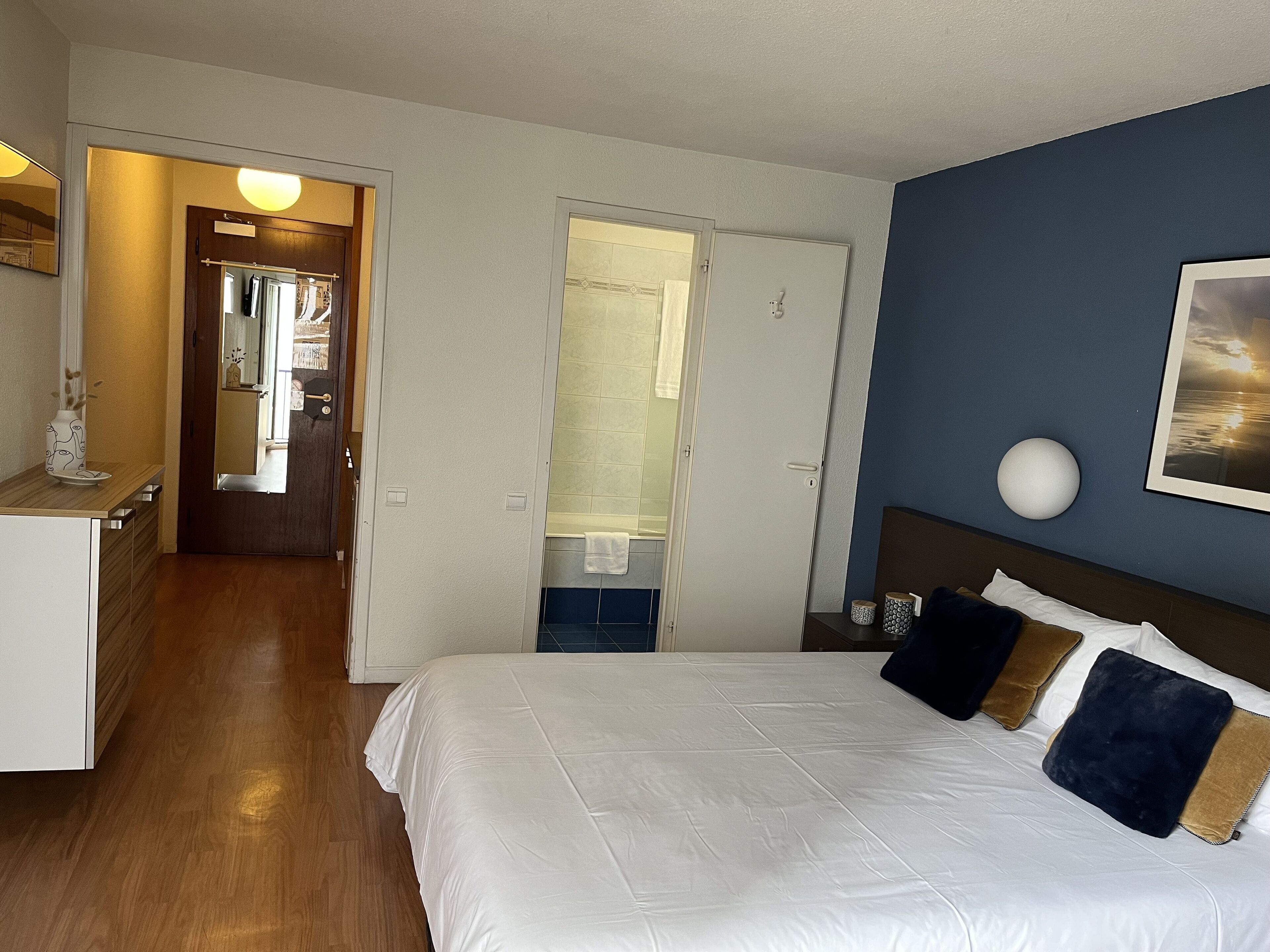 Et hotelværelse med seng, skrivebord, spejl og dør til badeværelse.
