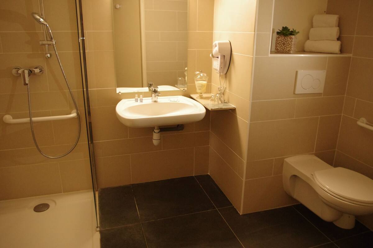 A bathroom with a shower, sink, toilet, and a shelf with towels and a plant.