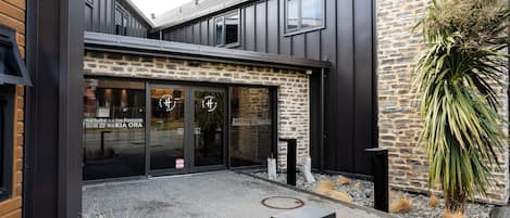 A modern building with a stone facade, large glass windows, and a small courtyard with a planter and a metal bench.