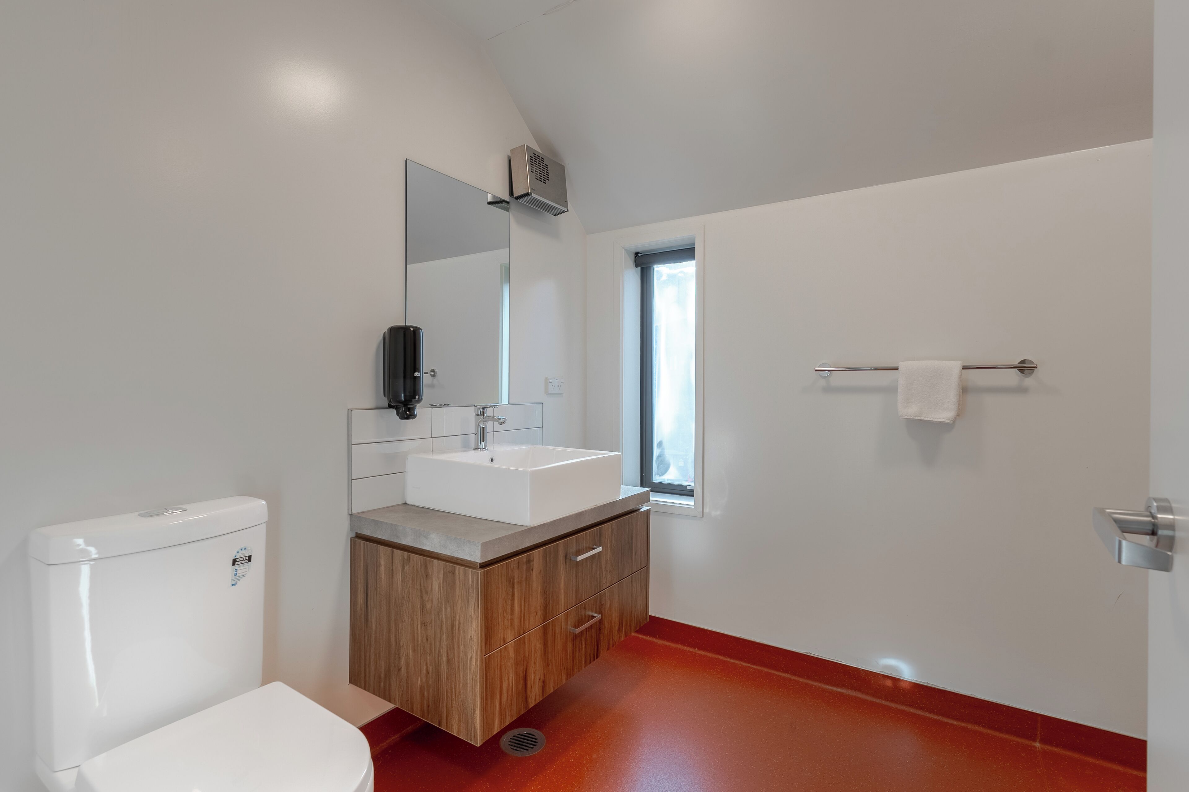 A modern bathroom with a white toilet, a wooden vanity with a sink, and a mirror.