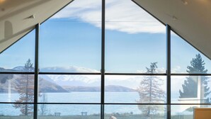 Una habitación con ventanas amplias que ofrecen vistas a un lago, montañas y árboles.