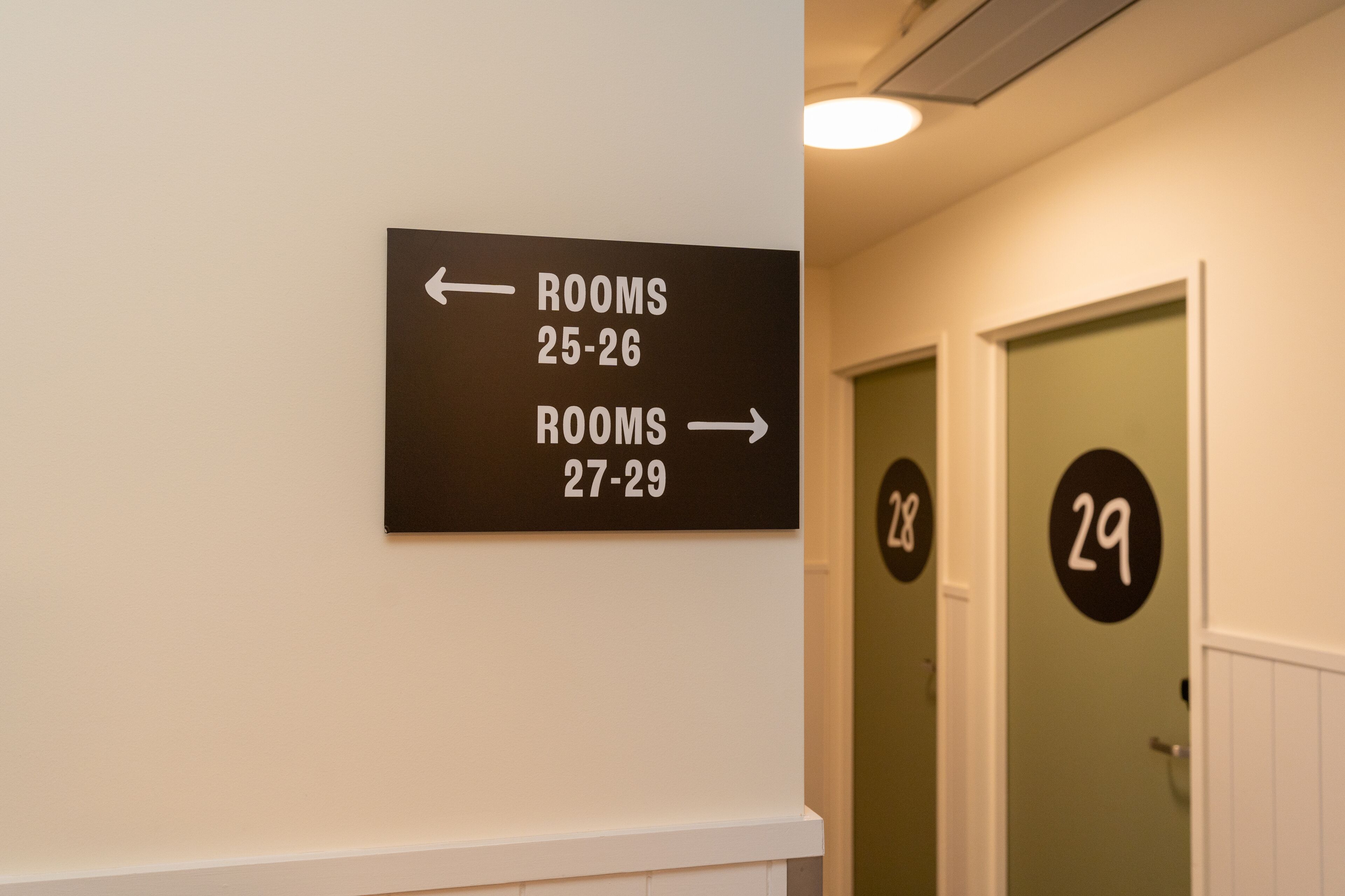 A hallway with directional signs indicating rooms 25-26 to the left and rooms 27-29 to the right.