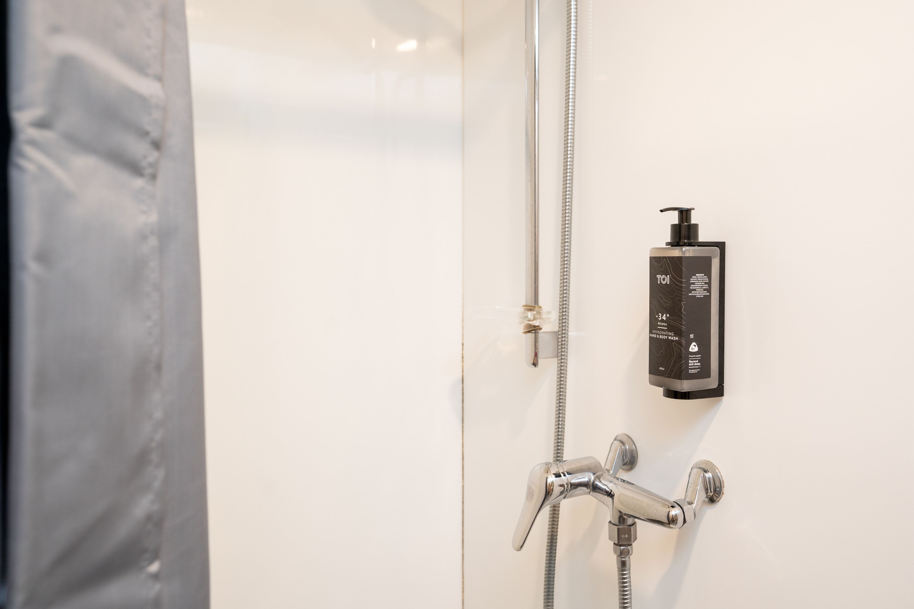 Een badkamer met een douche, een handdouche en een zeepdispenser op de muur.