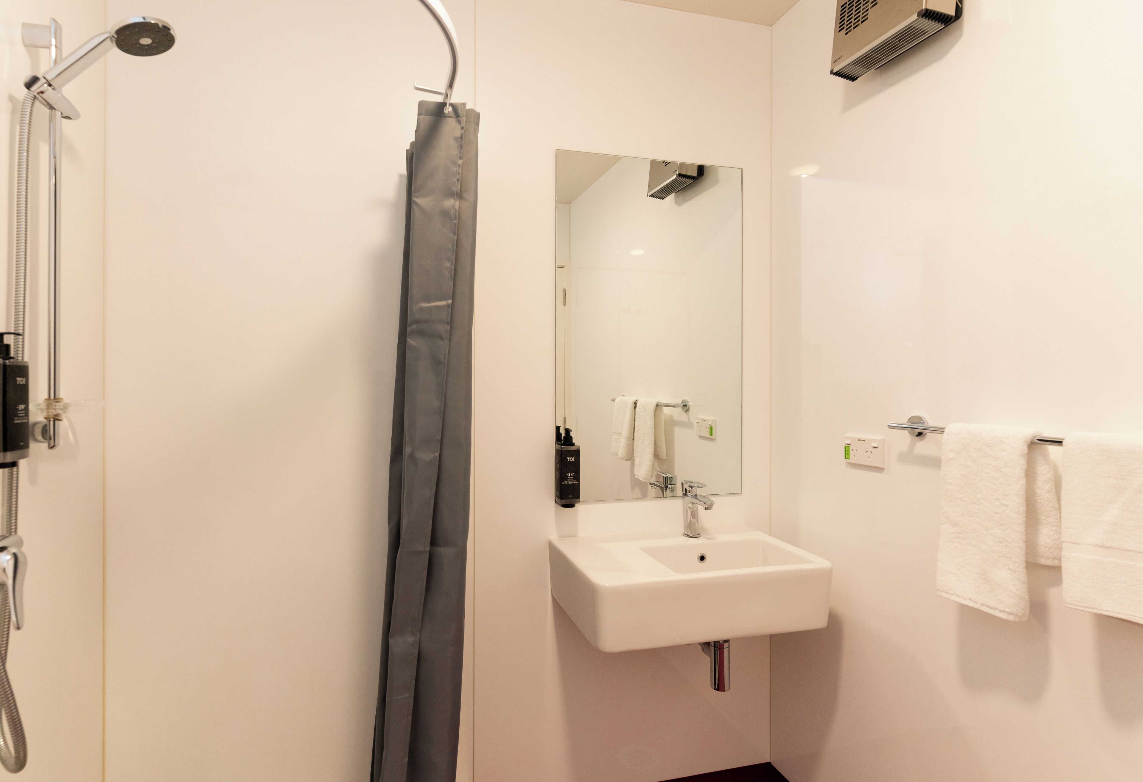 A modern bathroom with a shower, a sink, a mirror, and a towel rack.