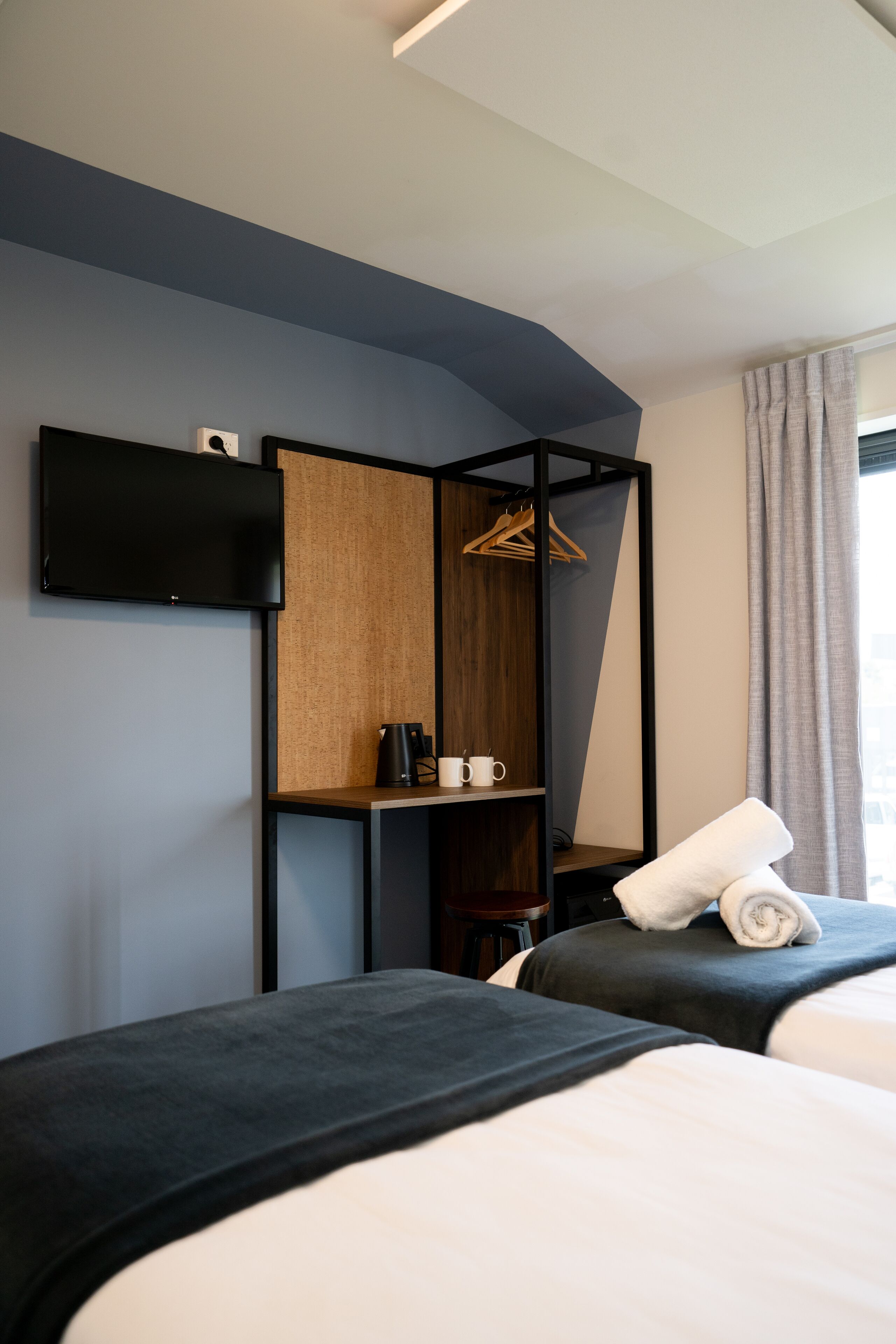 Hotelkamer met twee bedden, een aan de muur bevestigde televisie, een houten plank met een koffiezetapparaat en een kledingroede.