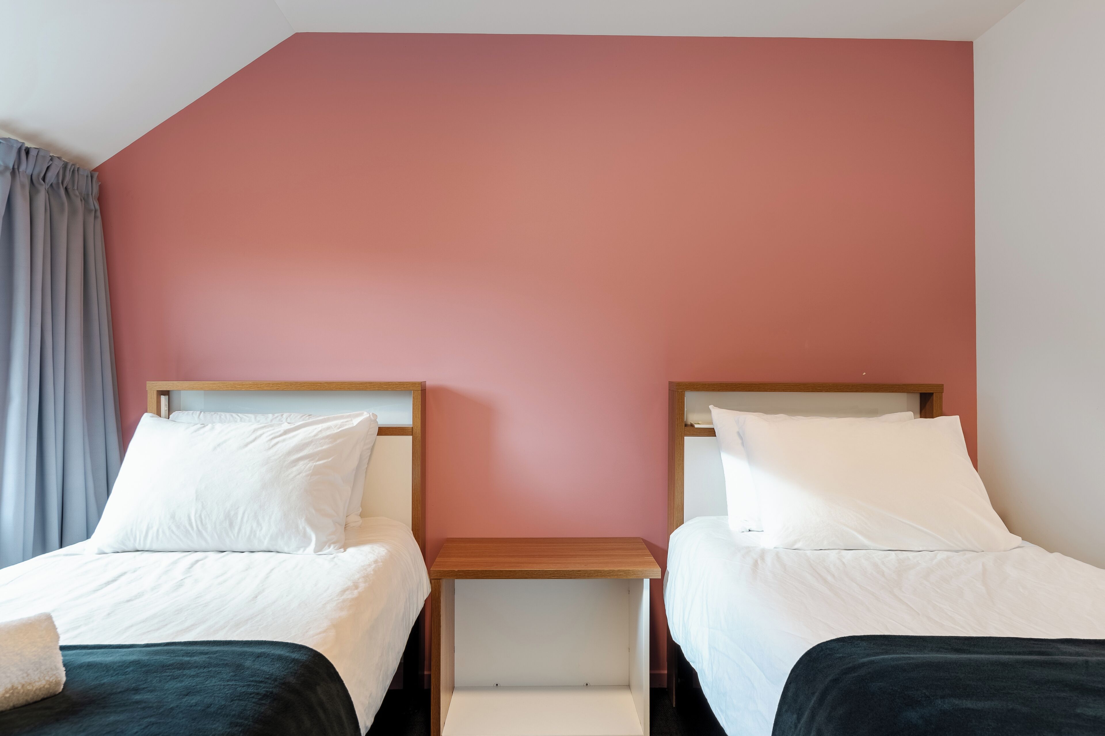 Camera d'albergo con due letti, un comodino in legno e una parete rosa.