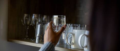 A hand reaching for a glass on a shelf with various glassware.