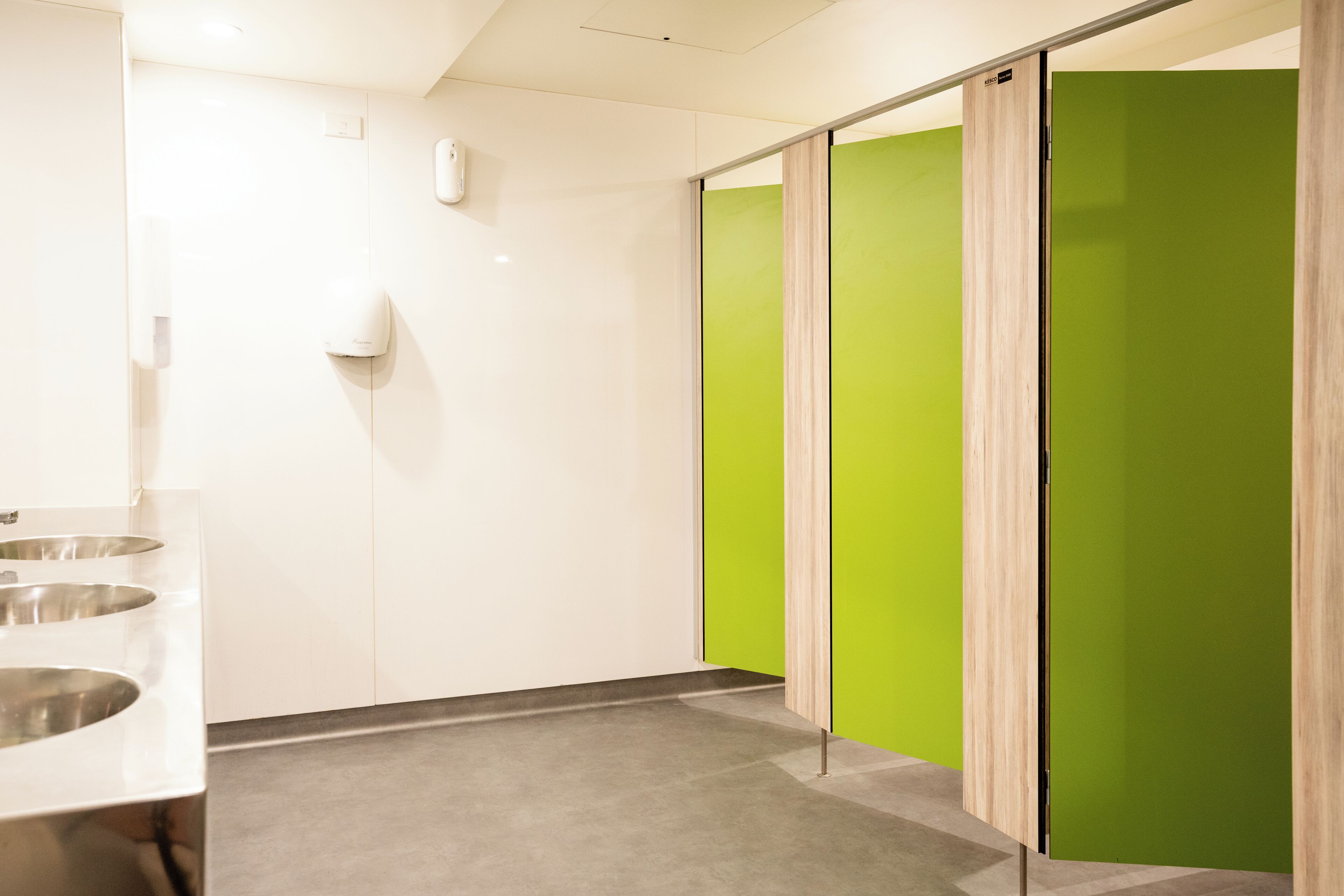 A restroom with a white wall, a green partition, and a sink with a mirror.