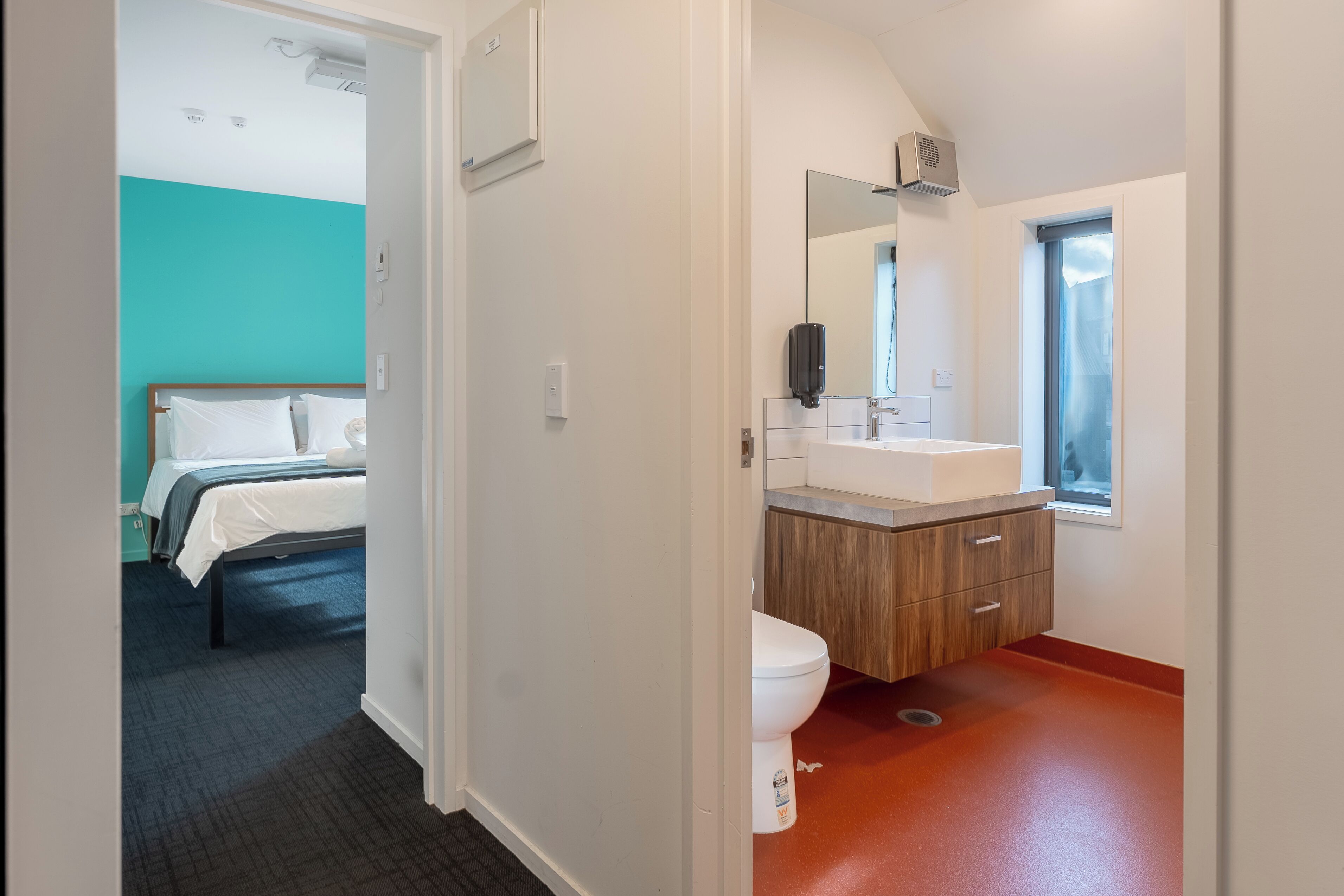 A modern hotel room with a bed, a bathroom with a sink and mirror, and a view of the outside.