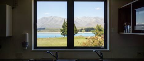 A kitchen with a double sink and a large window overlooking a lake and mountains.
