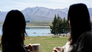 Dos personas sentadas junto a una ventana con vista a un lago y montañas.
