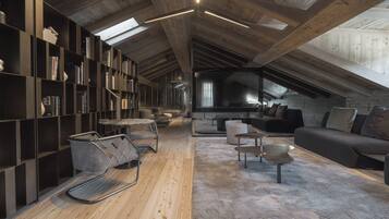 A loft-style room with a sloped ceiling, built-in bookshelves, a sofa, a coffee table, and a patterned rug.