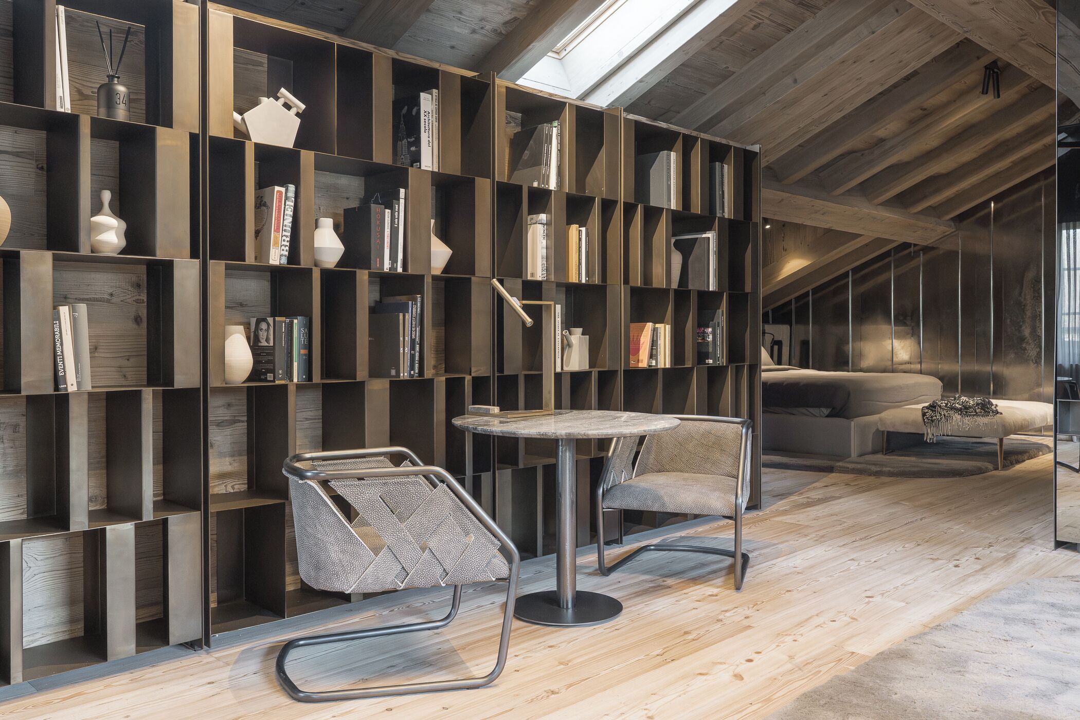 Un interior moderno con una estantería de madera, dos sillones, una mesa redonda y un sofá en un espacio tipo loft.