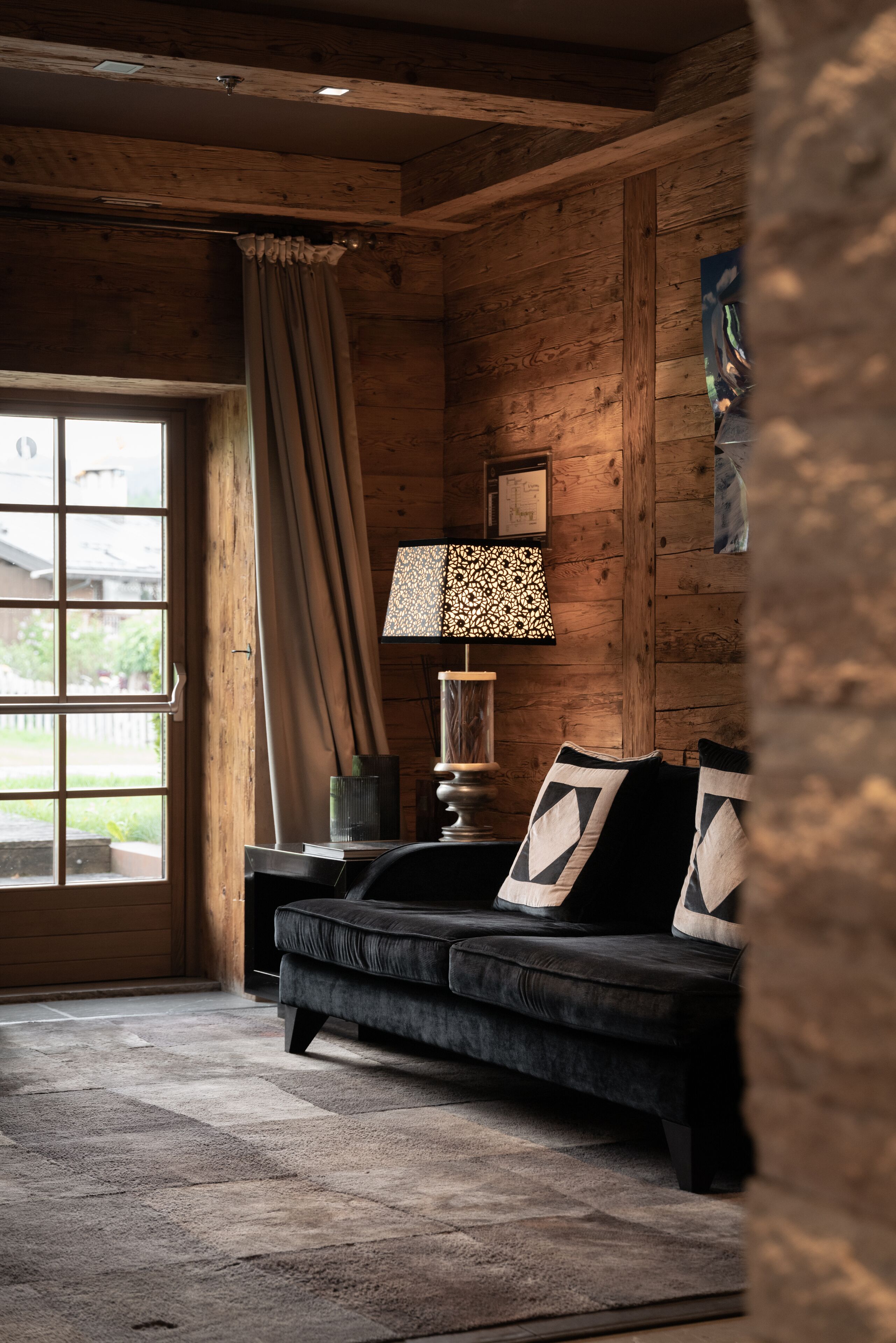 Ein gemütliches Zimmer mit einem dunklen Sofa, einer Lampe und Blick durch eine Glastür.