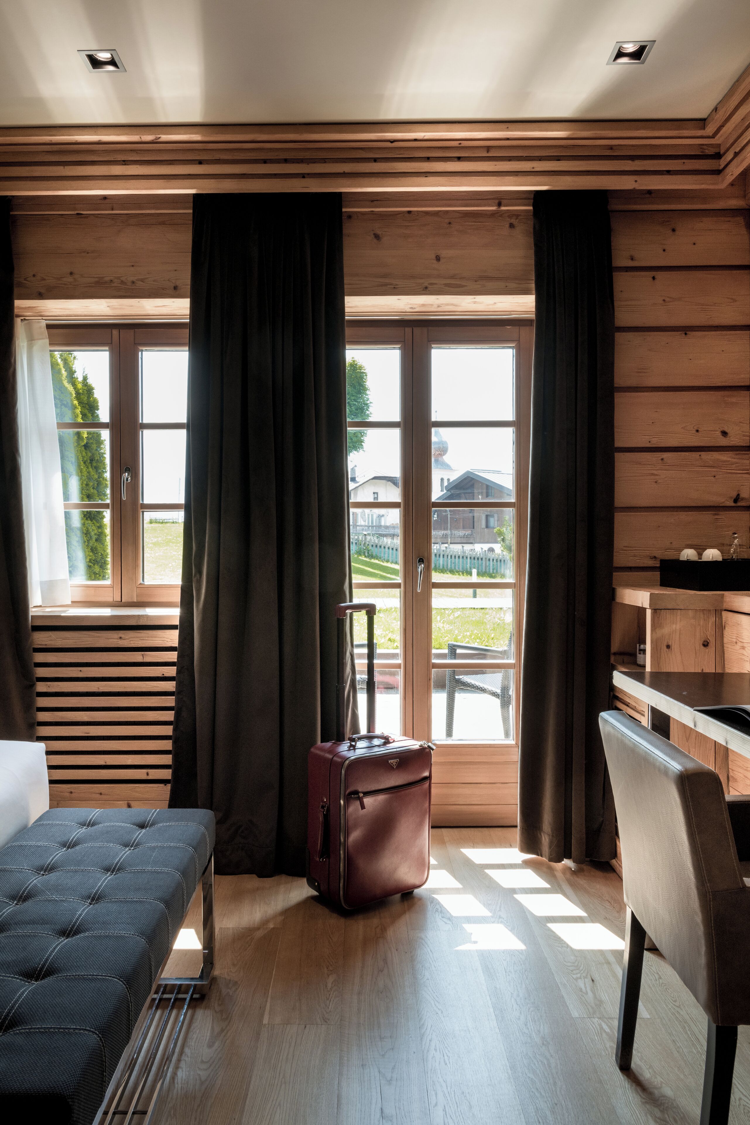 Une chambre avec un lit, un bureau, une valise et une vue sur l’extérieur, visible à travers une porte vitrée.