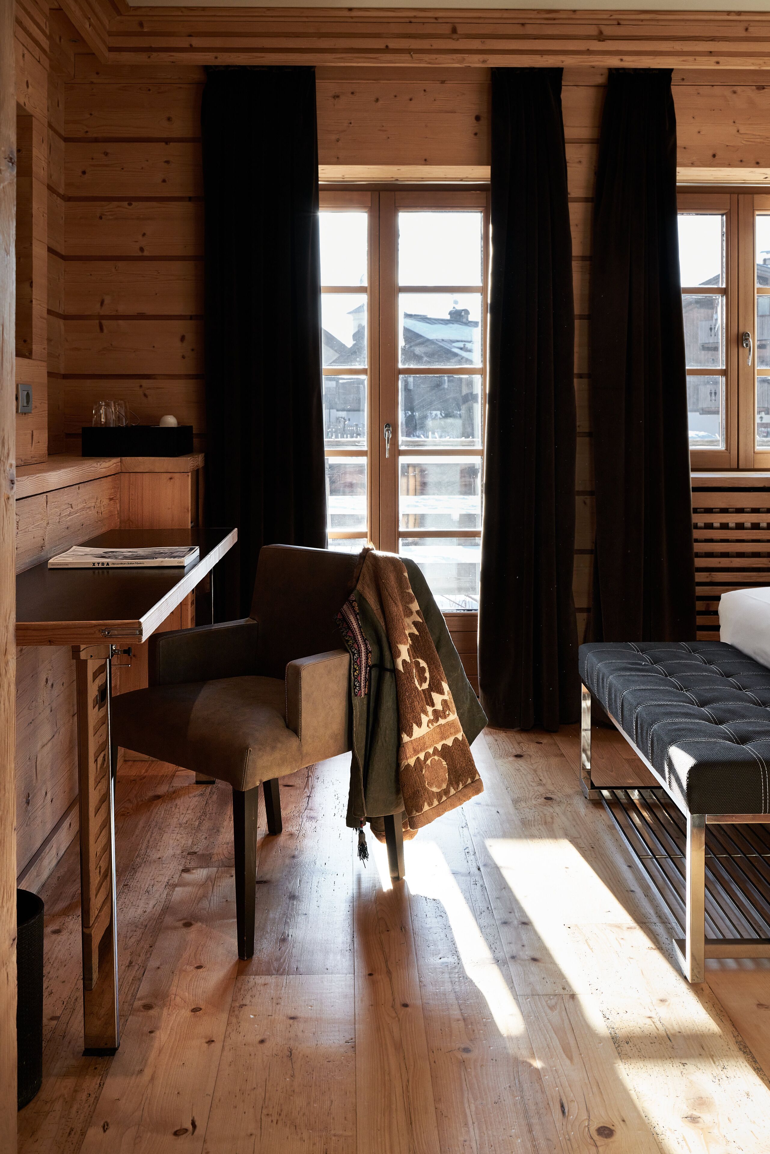 Quarto de cabana de madeira com cama, escrivaninha e janela com cortinas.
