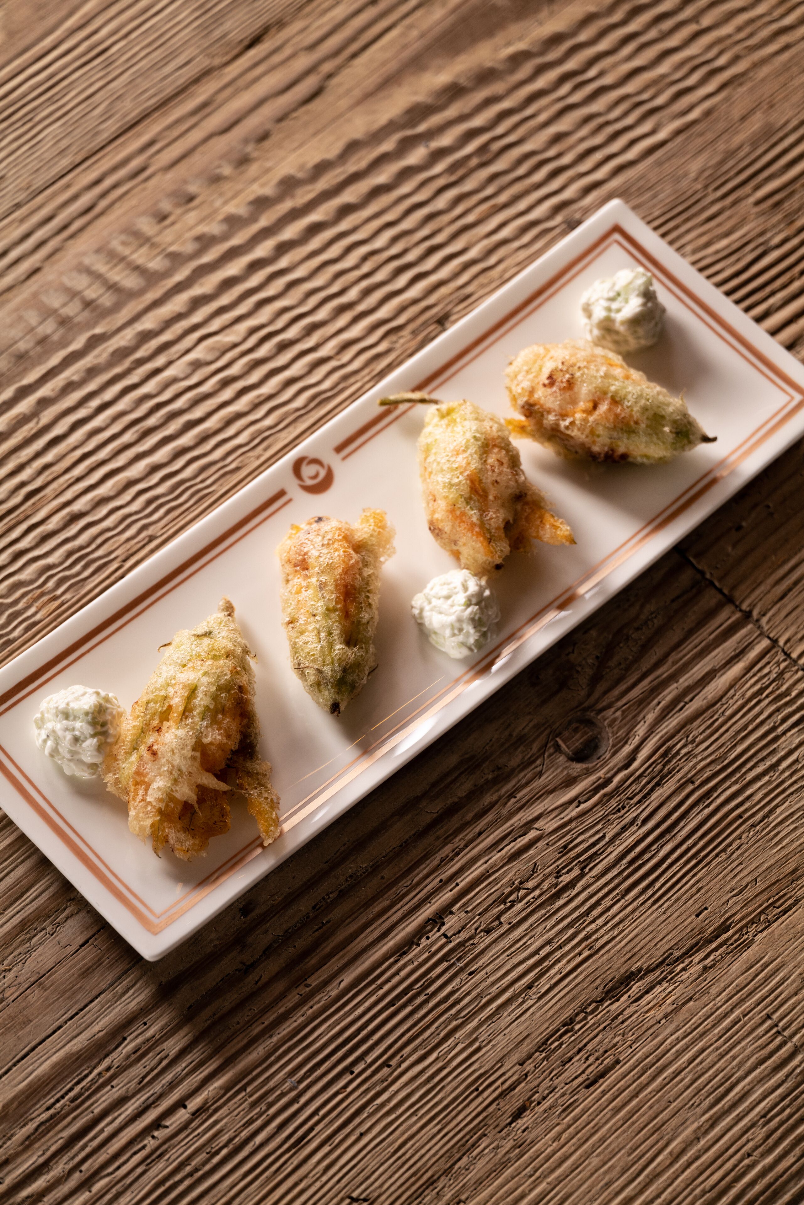 Une assiette rectangulaire contenant trois morceaux d’aliments panés et une cuillerée de crème, le tout posé sur une table en bois.