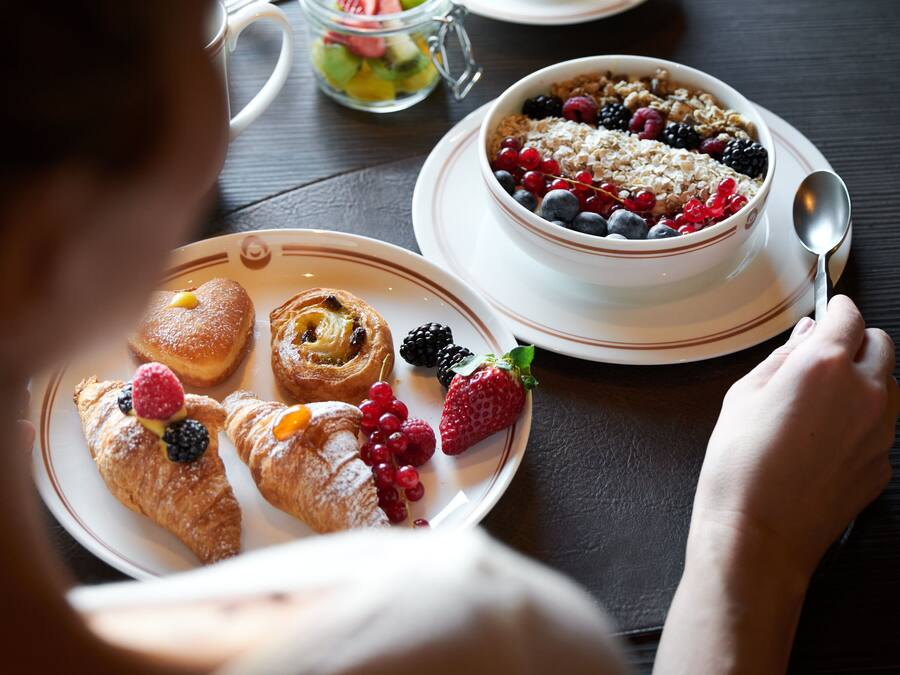 A dining table with a teapot, a bowl of cereal with berries, and croissants with berries.