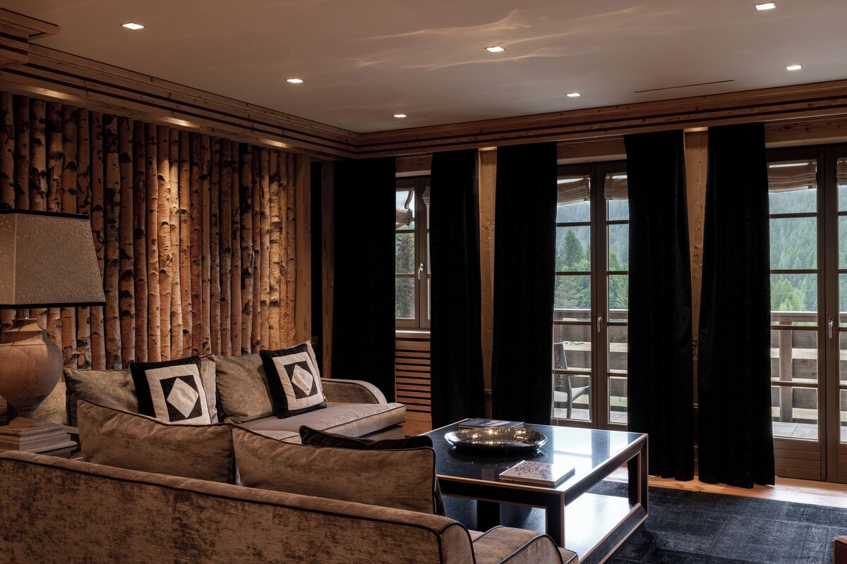 Una sala de estar con un sofá, una mesa de centro y una lámpara. Hay cortinas y una ventana con vistas a árboles.