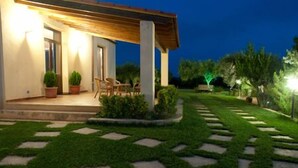 A well-lit outdoor area with a covered seating area, a pathway with stepping stones, and a lawn. - Le Foglie d'Argento (Caltabellotta)