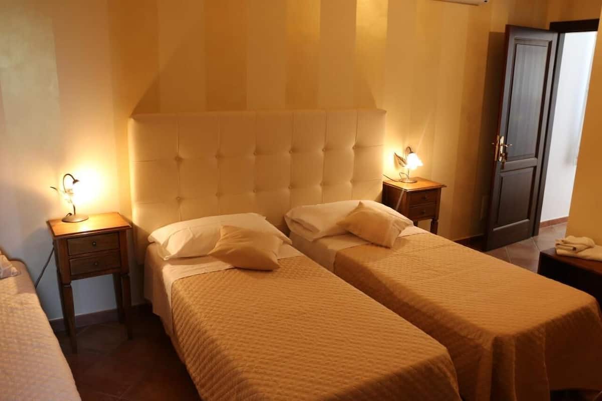 A hotel room with two single beds, a wooden nightstand with a lamp, and a wardrobe.